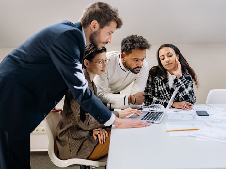 An instructor coaching three colleagues around a laptop
